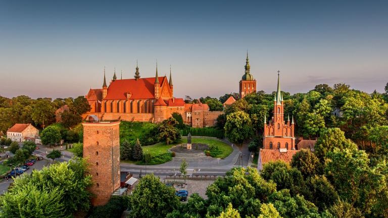 Great view of the beautiful city of Frombork located in Warmia, Poland. Cathedral Hill among trees at sunset shutterstock_2209500047.jpg