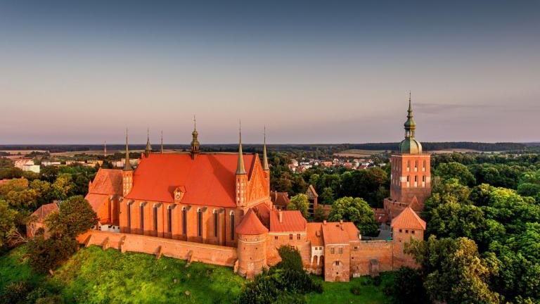 Great view of the beautiful city of Frombork located in Warmia, Poland. Cathedral Hill among trees at sunset shutterstock_2209500049.jpg